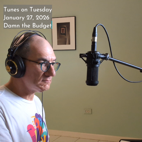 Photo of Oren Levine singing into a recording microphone suspended in front of his face. Text at top left reads 'Tunes on Tuesday January 27, 2026 Damn the Budget'