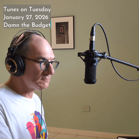 Photo of Oren Levine singing into a recording microphone suspended in front of his face. Text at top left reads 'Tunes on Tuesday January 27, 2026 Damn the Budget'